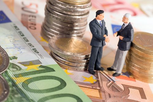 Foto: Zwei kleine Figuren stehend auf Geldscheine umringt von Münzen 